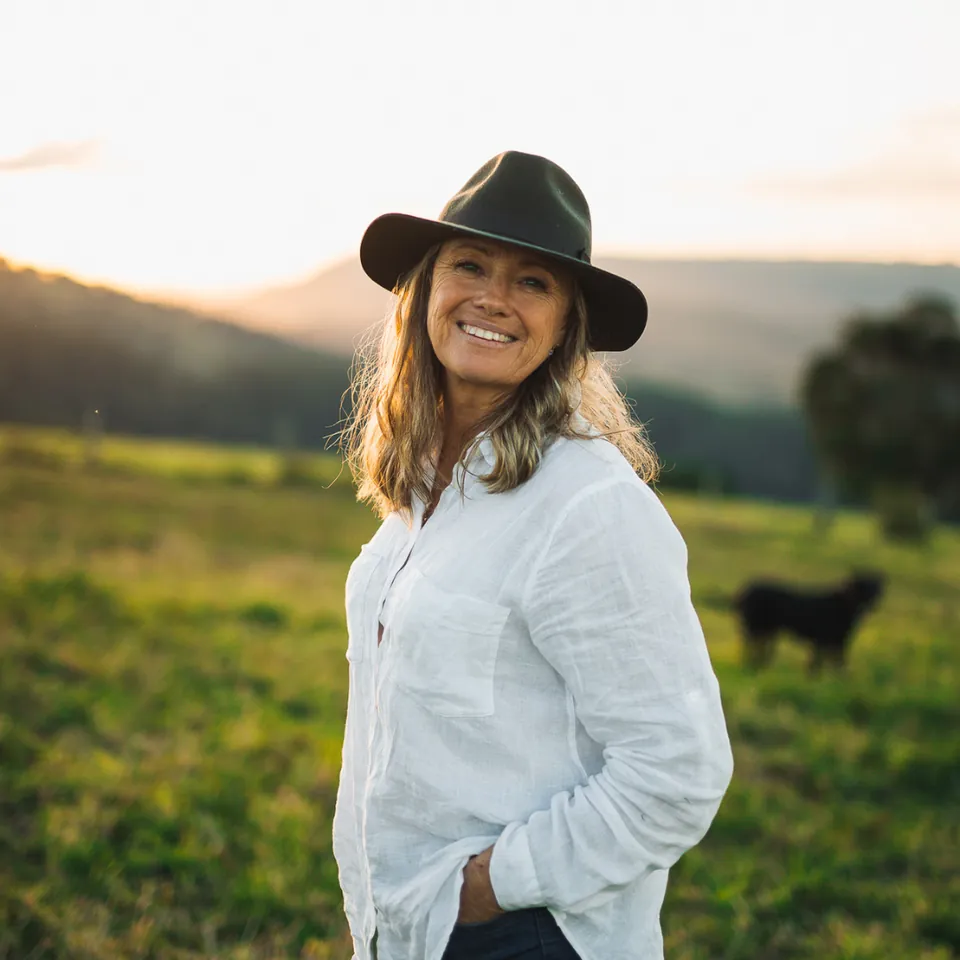Cyndi in a wide-brim hat standing in a green paddock at sunset